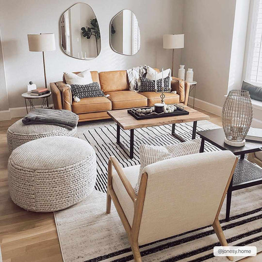 Angus rug in a customer's living room with a tan leather sofa, knitted poufs and irregular wall mirrors