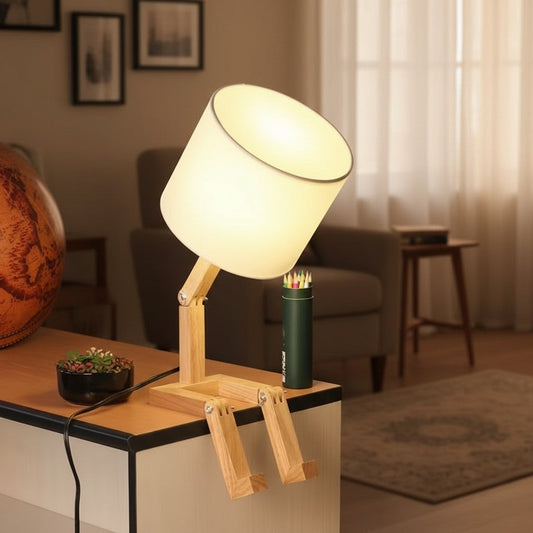 Wooden figure lamp on a dark side table with a pencil pot and framed art on the wall behind