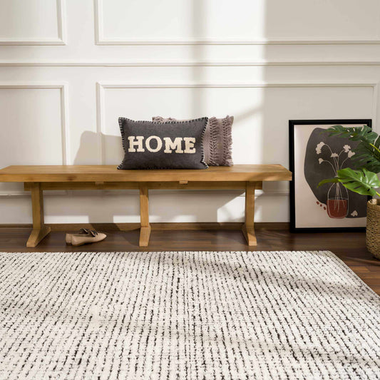 Wooden bench with 'HOME' pillow in a room with a rug and wall art.