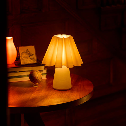 Ruff Lamp glowing on a round wooden side table next to a stack of books and a small framed picture