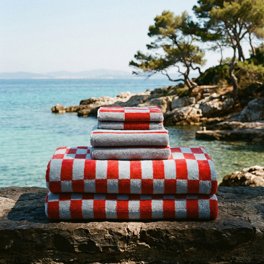 Stack of red and white checked Pietra towels on a rock above a turquoise cove