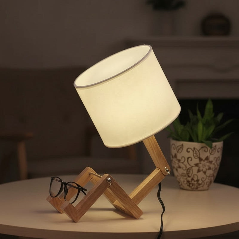 Folding wooden figure lamp lit warm on a table beside a pair of glasses and a potted plant