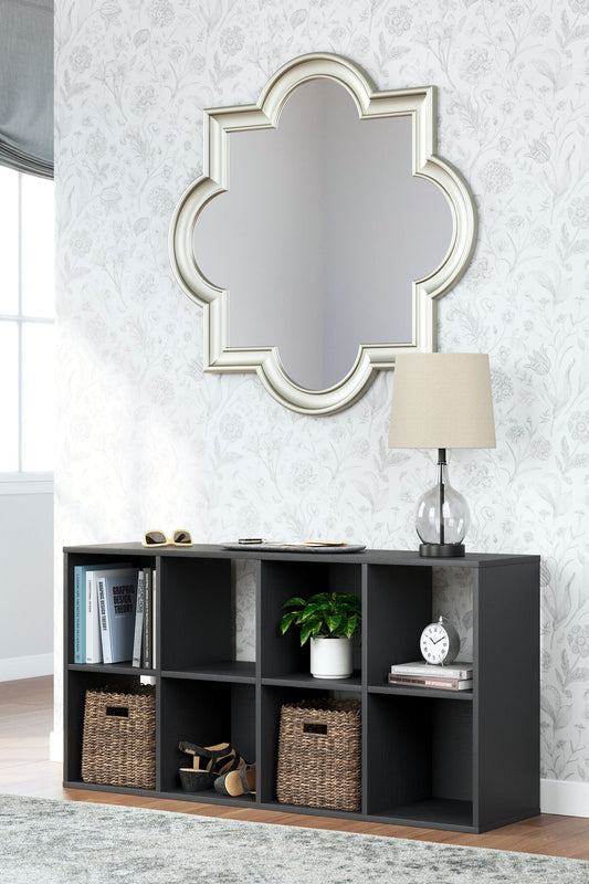 Black eight-cube storage unit laid on its side as a console holding books, a plant, a clock and two woven baskets, beneath a mirror and lamp
