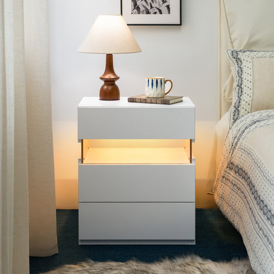 White nightstand with illuminated interior next to a bed in a bedroom setting.