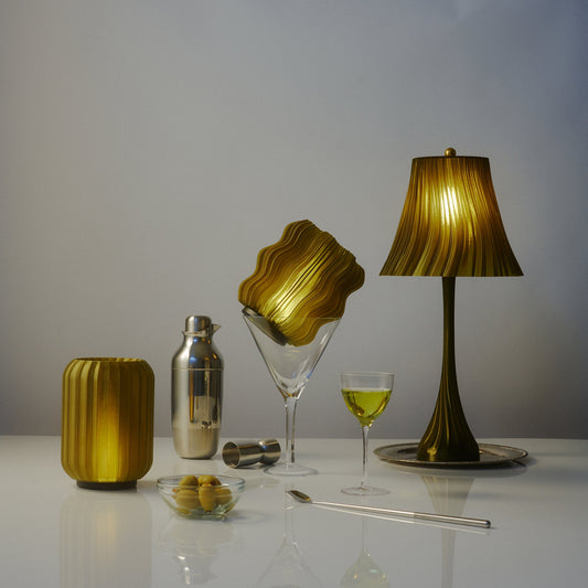 Olive Oil Mini Wavy lamp lit on a white table among cocktail glasses and a shaker