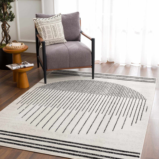 Angus rug on a wood floor beside a grey armchair and a wooden side table by a sunlit curtain