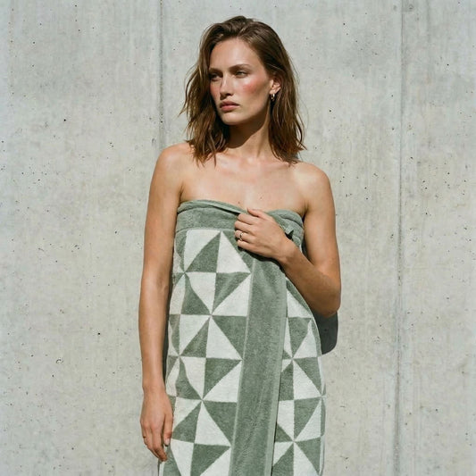 Woman wrapped in a sage and white triangle-print bath sheet against a concrete wall