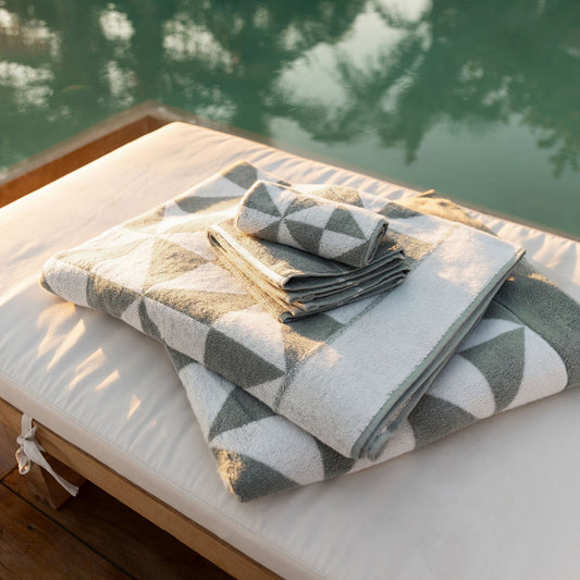 Folded stack of sage and ecru triangle-print towels on a bench beside a poolside deck