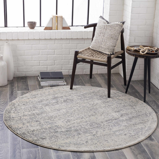 Round gray rug on a wooden floor with a chair and small table in the background.